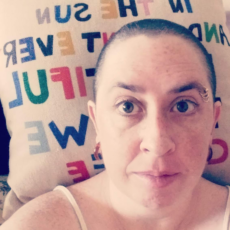 A selfie photo of Catherine looking at the camera. She has a shaved head and eyebrow rings on her left eyebrow. 