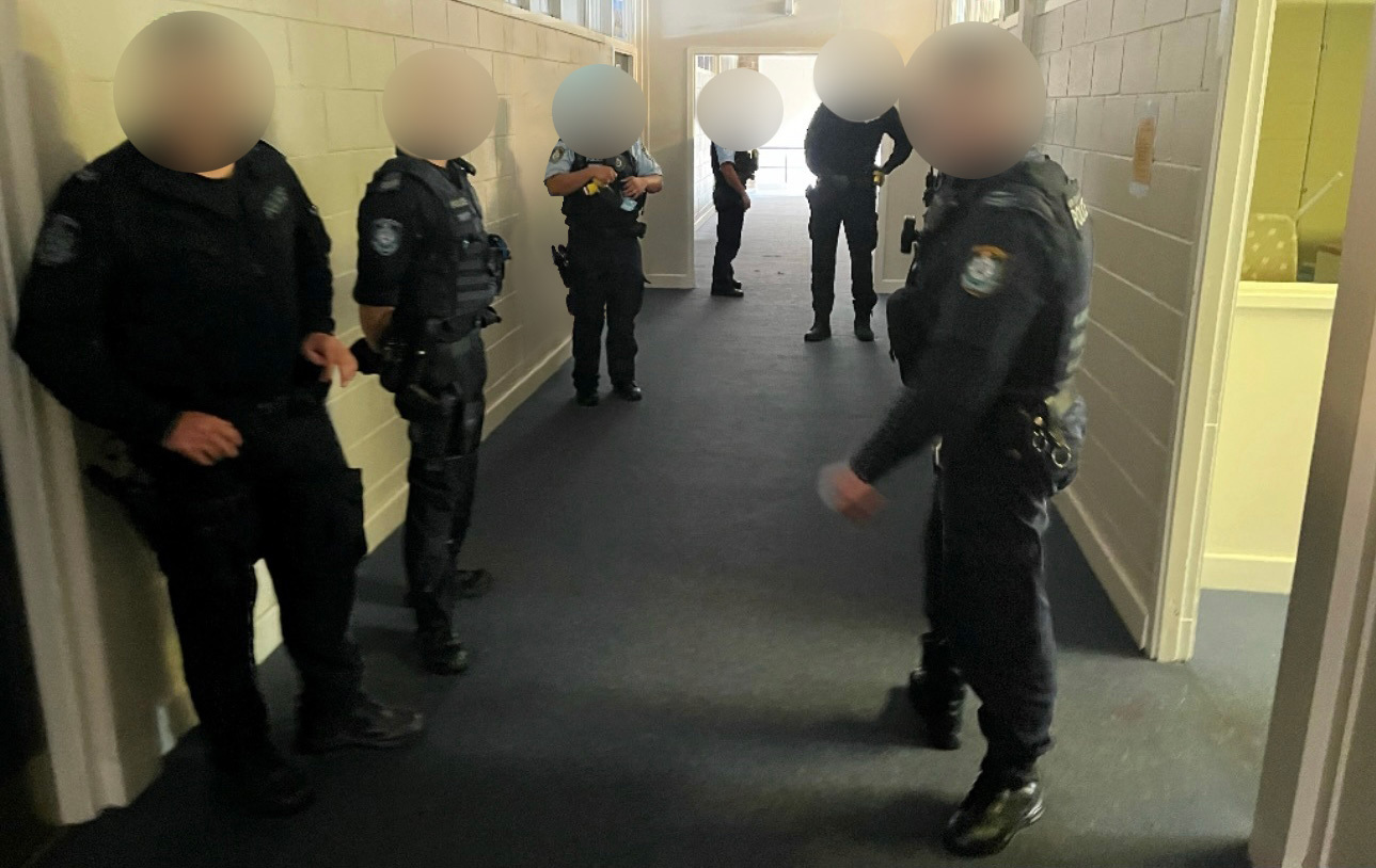 Image shows: Six police officers standing in a school corridor. Their faces and uniforms have been blurred to protect their identity.