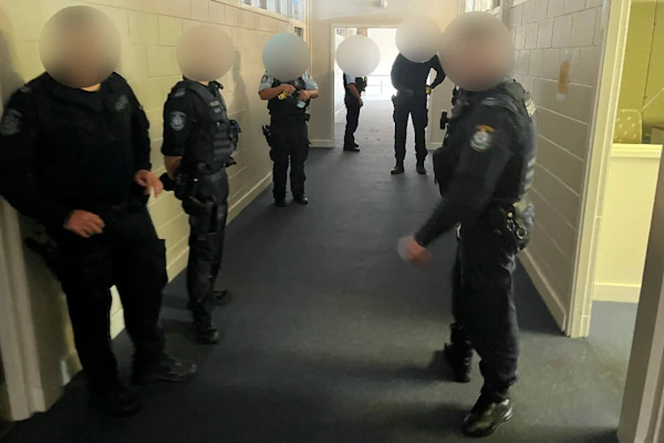 Image shows: Six police officers standing in a school corridor. Their faces and uniforms have been blurred to protect their identity.