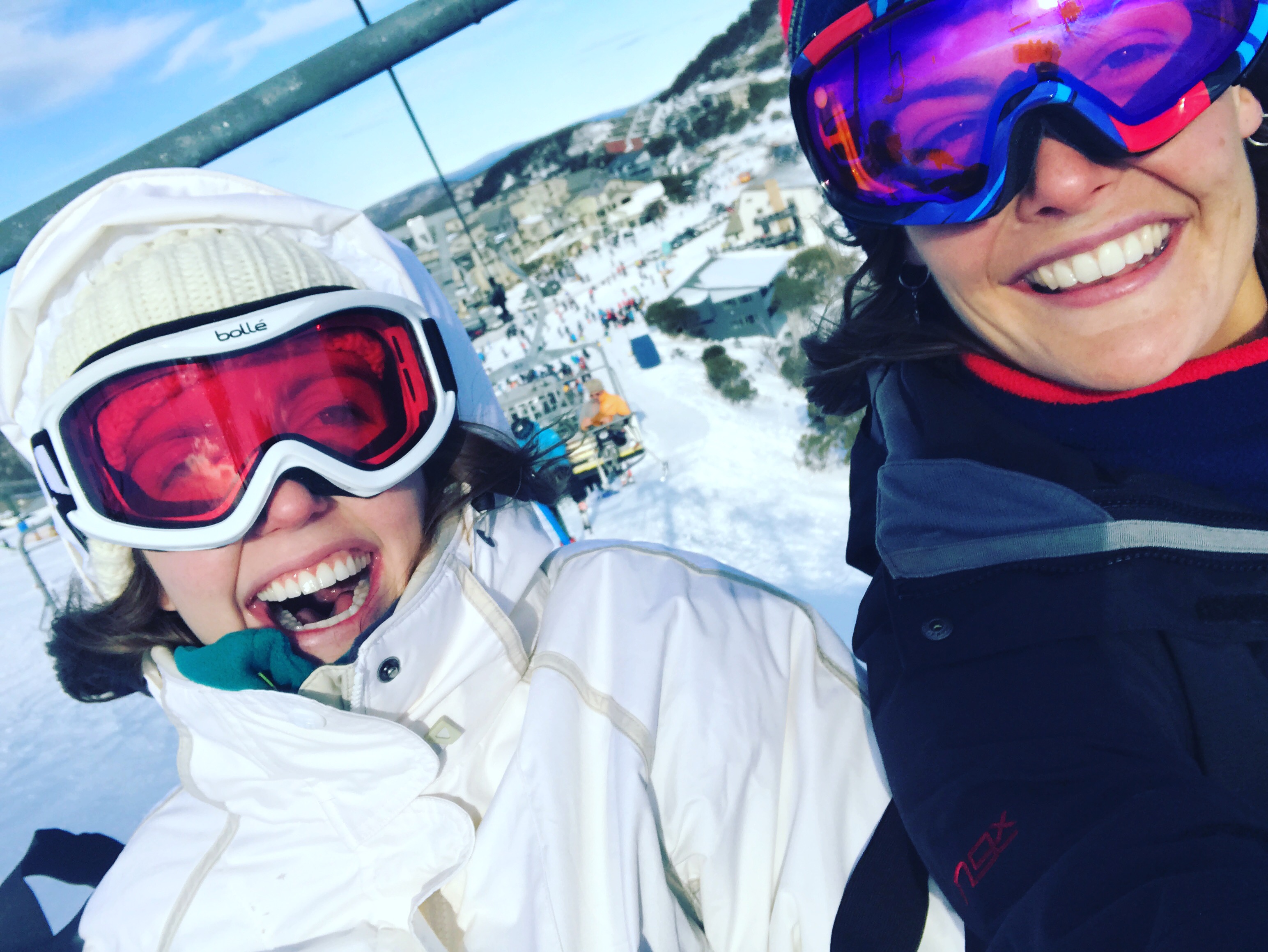 Sam is on a ski lift next to her Hireup support worker. They are both wearing ski goggles.