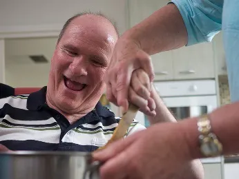 A support worker helping a man with disability cook for himself.