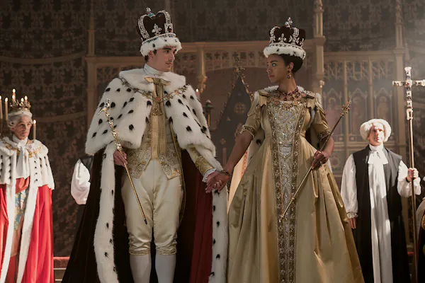 The characters of King George III and Queen Charlotte stand looking at one another in regal dress.