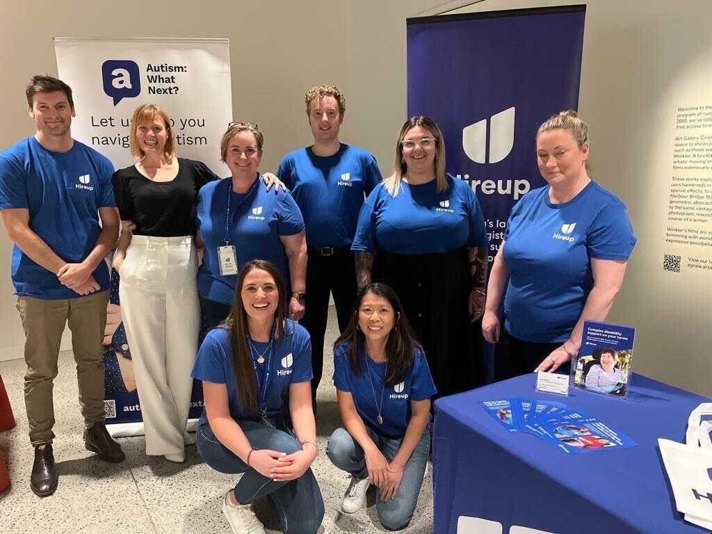 Julian is standing in the middle of a group of Hireup support office staff. Everyone is wearing blue Hireup t-shirts.