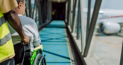 A man in a wheelchair is assisted down an air bridge toward a plane.