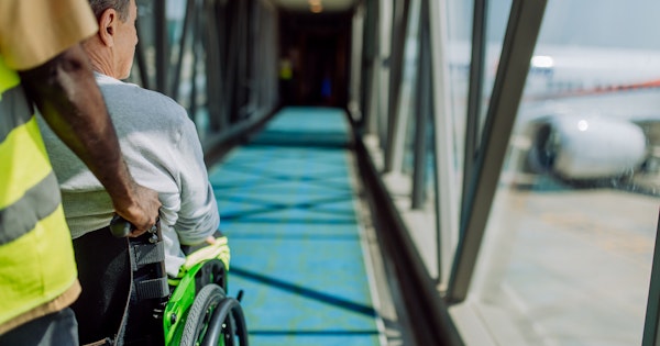 A man in a wheelchair is assisted down an air bridge toward a plane.