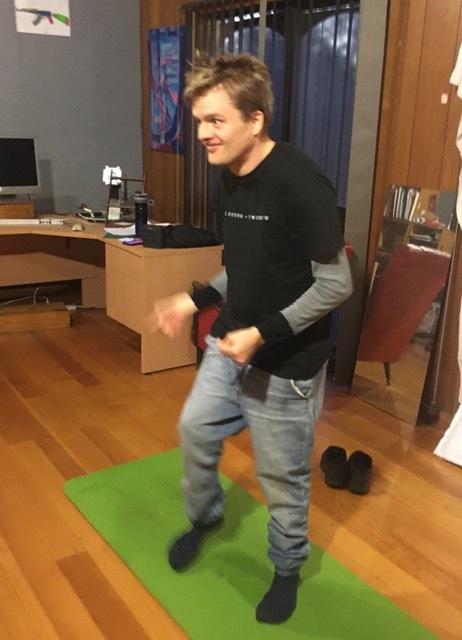 Julian who has short dark hair is dancing. He is on a yoga mat and is wearing socks with no shoes.