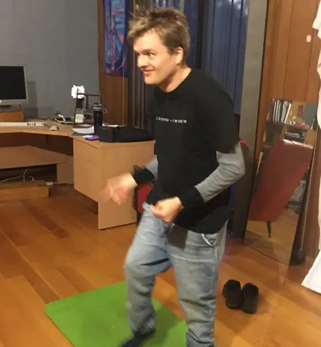 Julian who has short dark hair is dancing. He is on a yoga mat and is wearing socks with no shoes.