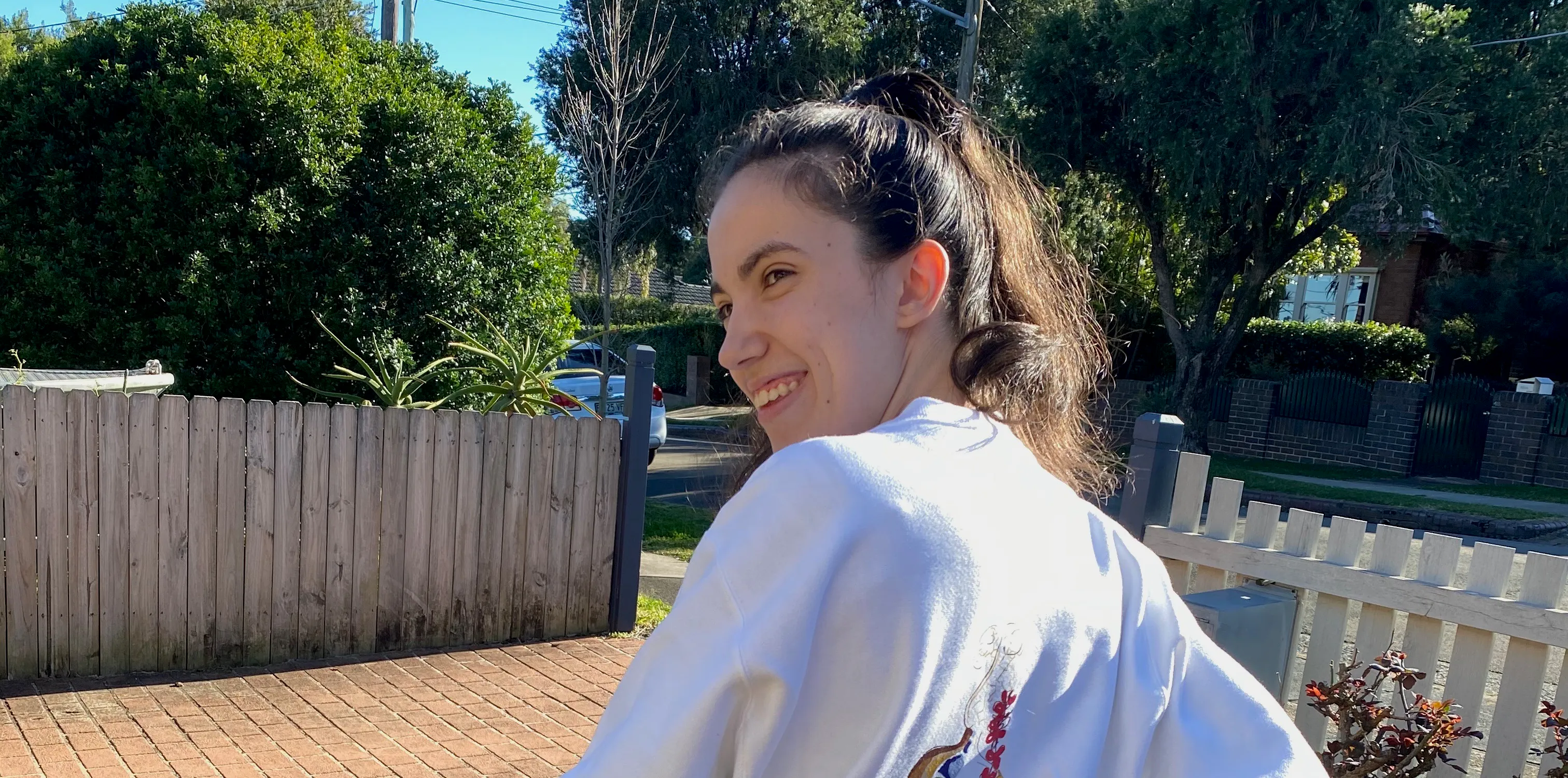 Hannah's hair is tied into a ponytail and she's wearing a jumper that has a colourful drawing depicted on it. The drawing is an outline of a woman and a branch of flowers used to represent scoliosis of the spine. Hannah is resting on her walker.