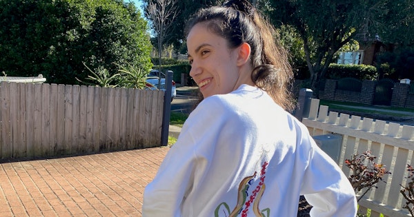 Hannah's hair is tied into a ponytail and she's wearing a jumper that has a colourful drawing depicted on it. The drawing is an outline of a woman and a branch of flowers used to represent scoliosis of the spine. Hannah is resting on her walker.