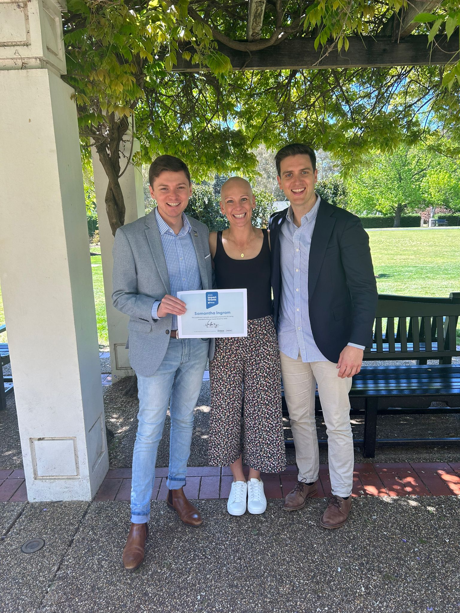 Hireup support worker Samantha is being presented a Impact Grants certificate by MLA Johnathan David and Hireup Co-CEO Jordan O'Reilly. They're in a garden.