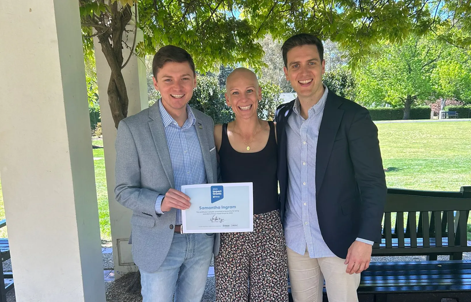 Hireup support worker Samantha is being presented a Impact Grants certificate by MLA Johnathan David and Hireup Co-CEO Jordan O'Reilly. They're in a garden.