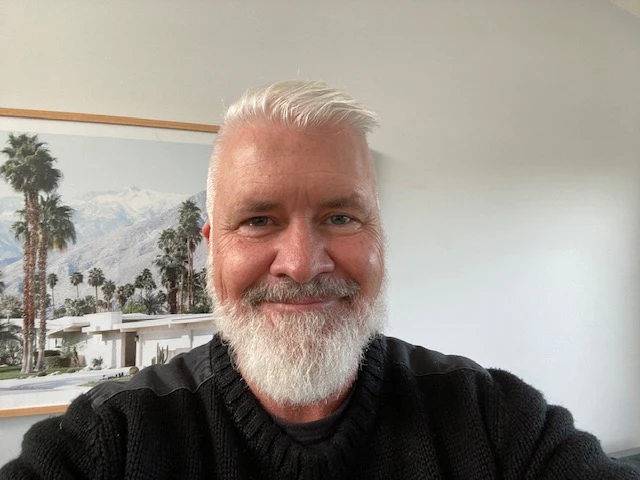 Rob is smiling, wearing a black jumper. He has short white hair and a white beard.