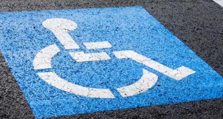 A disability parking sign is painted on a road. It's a stencil of a person in a wheelchair in a blue box. 