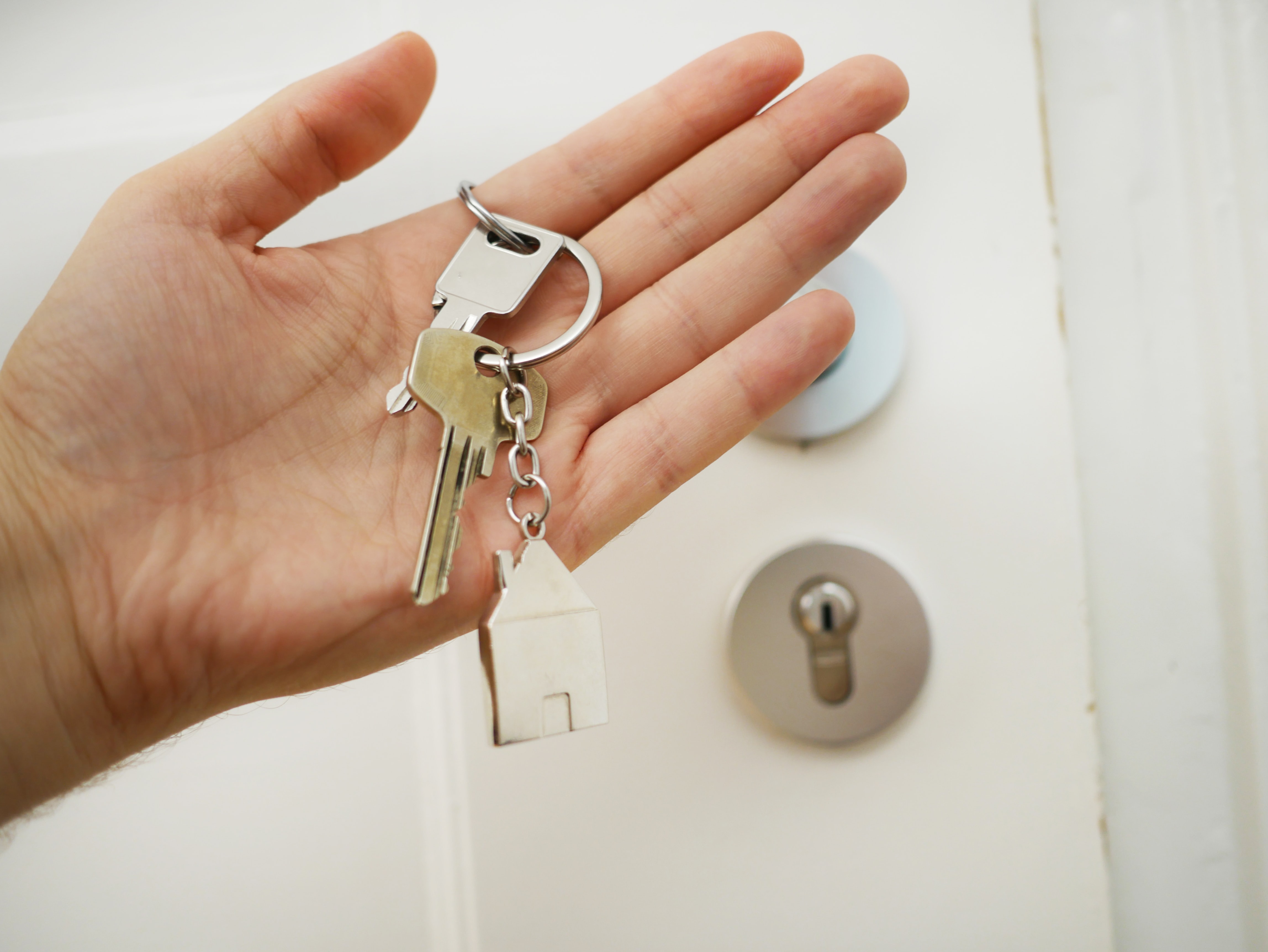A hand holds a set of house keys in front of a door. 