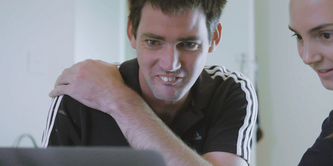 A man and a woman are sitting in front of a computer. They are both smiling. 