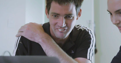 A man and a woman are sitting in front of a computer. They are both smiling.