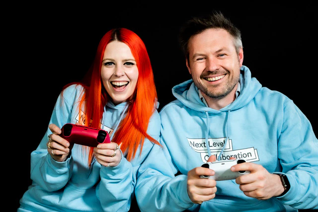 Next Level Collaboration founders Matt Harrison and Jess Rowling pose with gaming controls, wearing blue hoodies promoting their program.