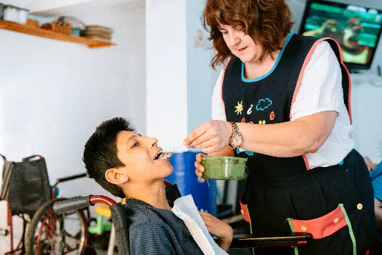 A support worker helping a boy eat a meal