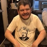 Todd has short hair and a beard. He's wearing a t-shirt with an image of American President Franklin D Roosevelt. The words 'For a new deal' surround the image. Todd is a wheelchair user.