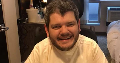 Todd has short hair and a beard. He's wearing a t-shirt with an image of American President Franklin D Roosevelt. The words 'For a new deal' surround the image. Todd is a wheelchair user.