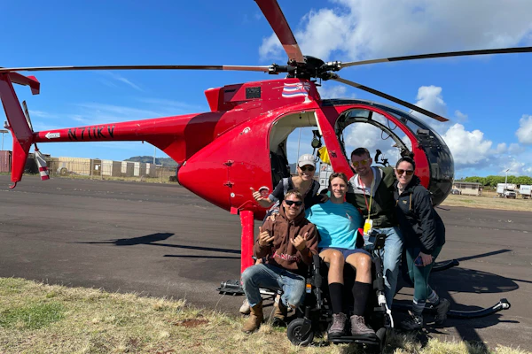 A group of friends, including wheelchair user Steve Ralph, pose in front of a red helicopter.
