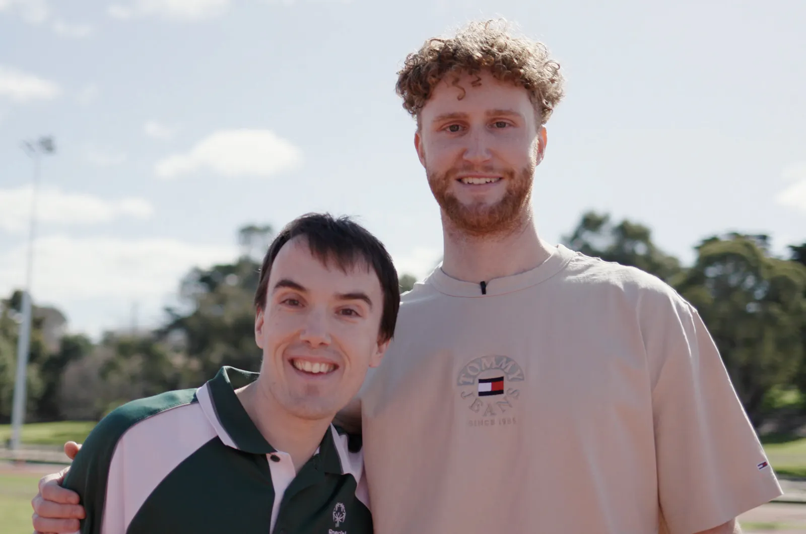 Hireup client Adrian is smiling as he stands beside his support worker Luke. They are at a running track.