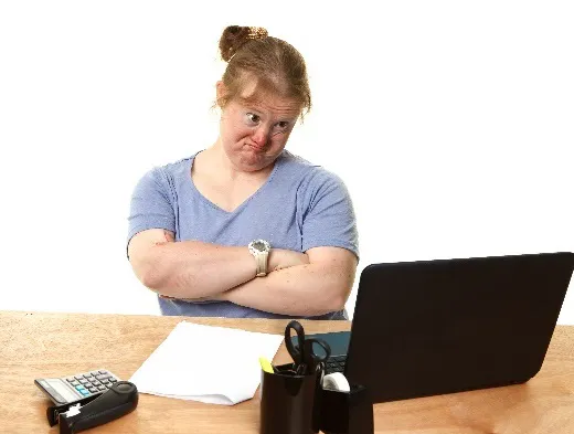 A woman frowning with her arms crossed and a computer in front of her