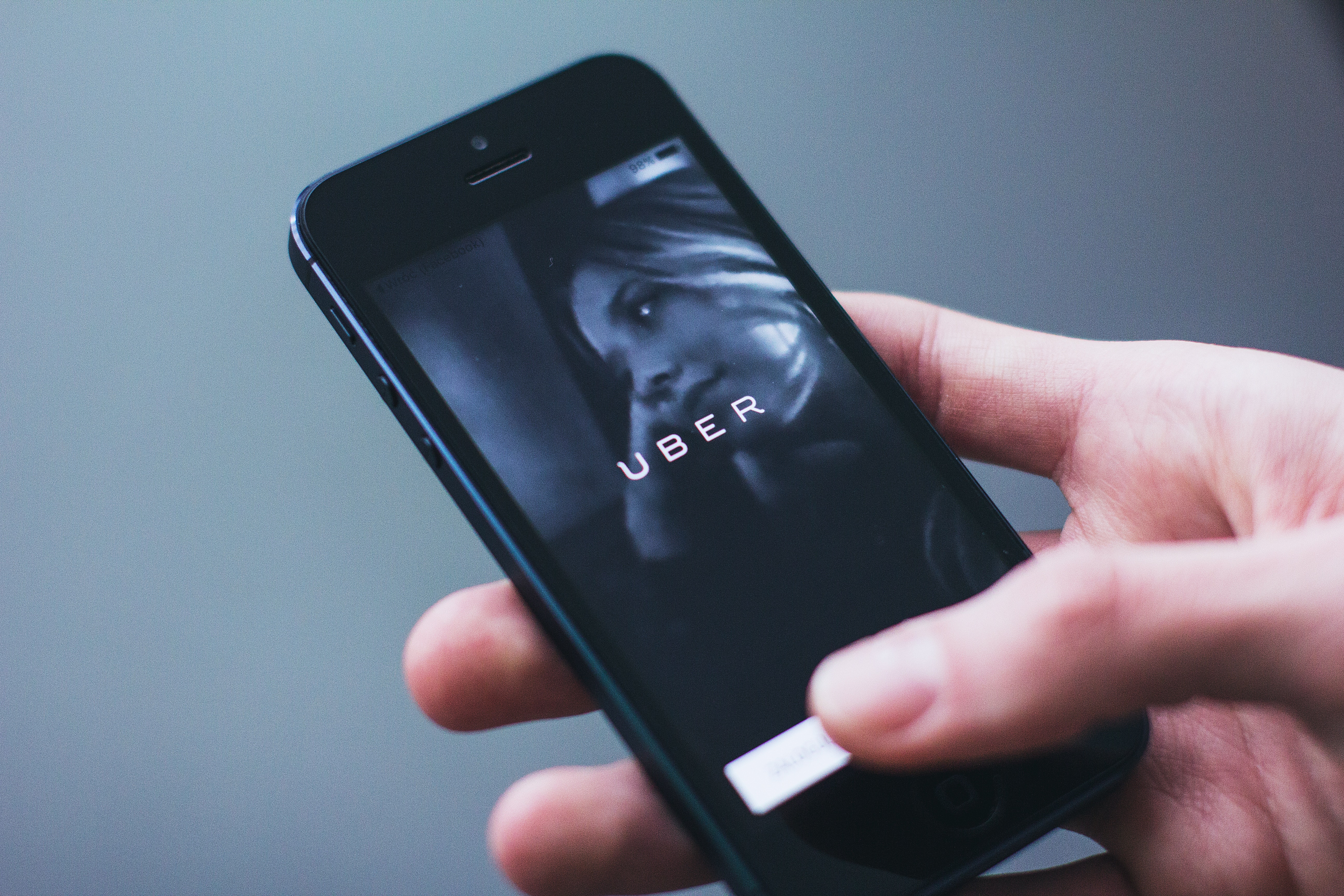 A hand holds a phone featuring the home screen of the Uber app. 