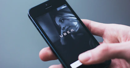 A hand holds a phone featuring the home screen of the Uber app.
