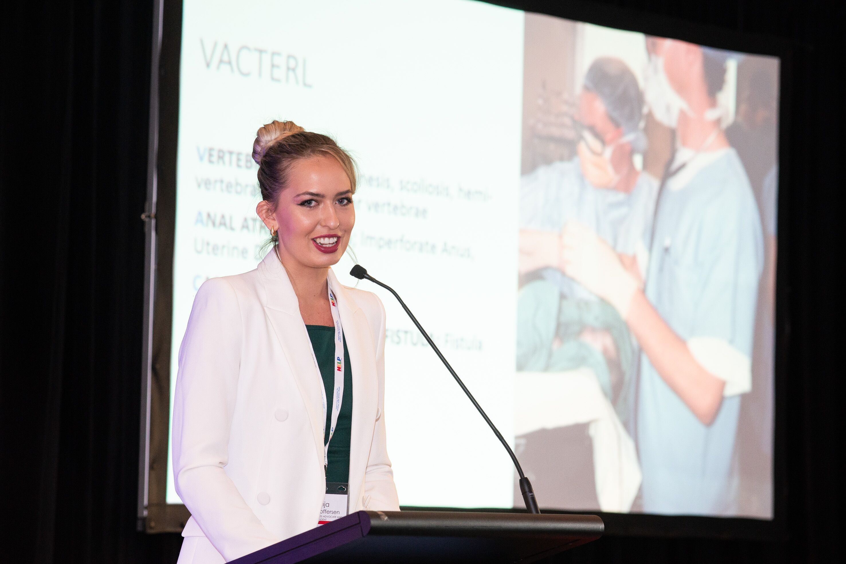 Anja wearing a white blazer is speaking in front of a slideshow.