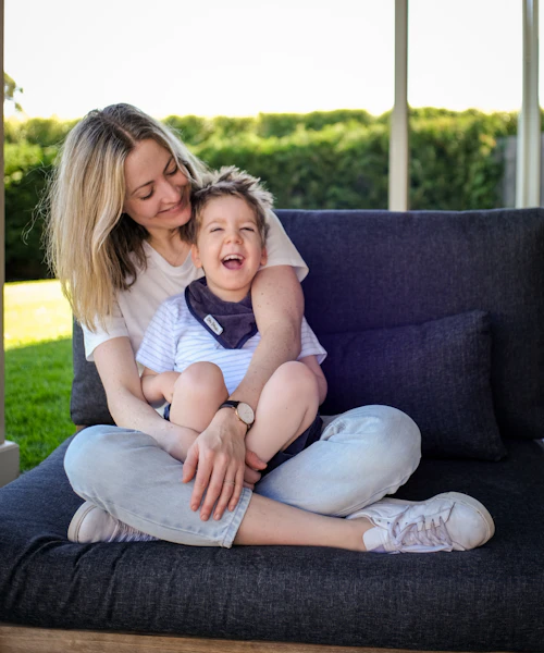 Mel is sitting on a couch with her son Arlo in her lap. They're both laughing.