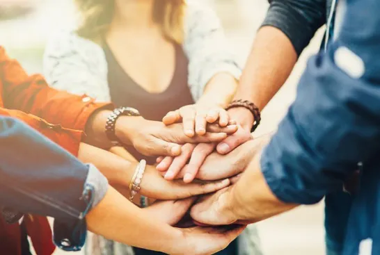 A group of people in a circle with their hands together.