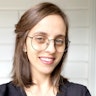 Liel Bridgford has shoulder-length brown hair and green eyes. She wears glasses, a golden heart locket and a dark top.