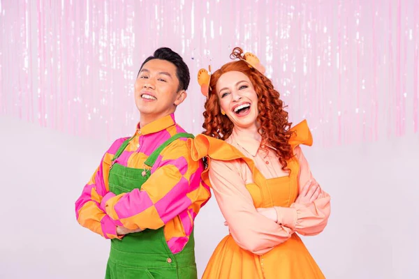 Emma Memma and Elvin Melvin, two children's entertainers dressed in bright clothing, smile at the camera.