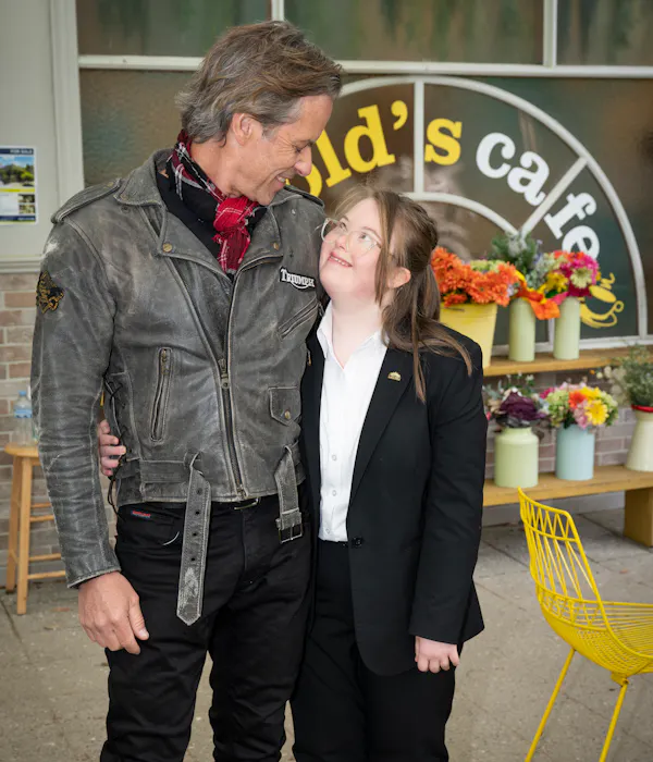 Actors Guy Pearce and Henrietta Graham pose arm in arm on the set of Neighbours. They are looking at each other and smiling.