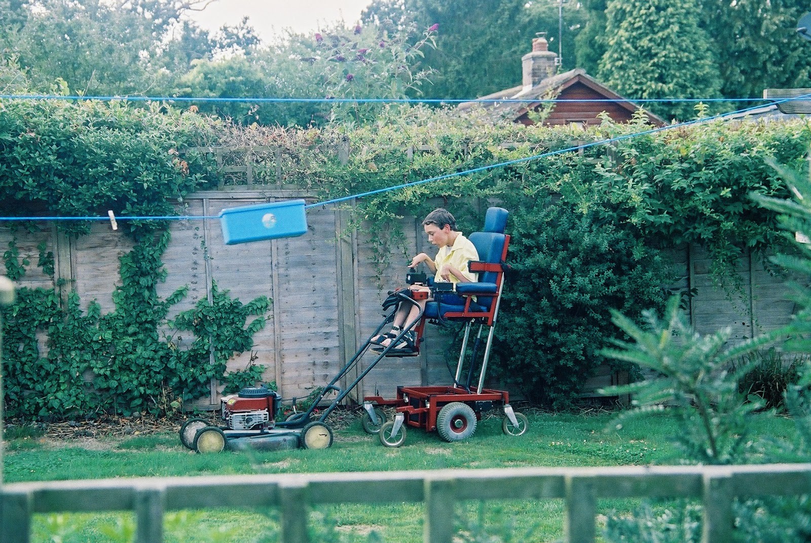Jordan's brother Shane is using a lawn mower. It is attached to his motorised wheelchair that is raised quite high.