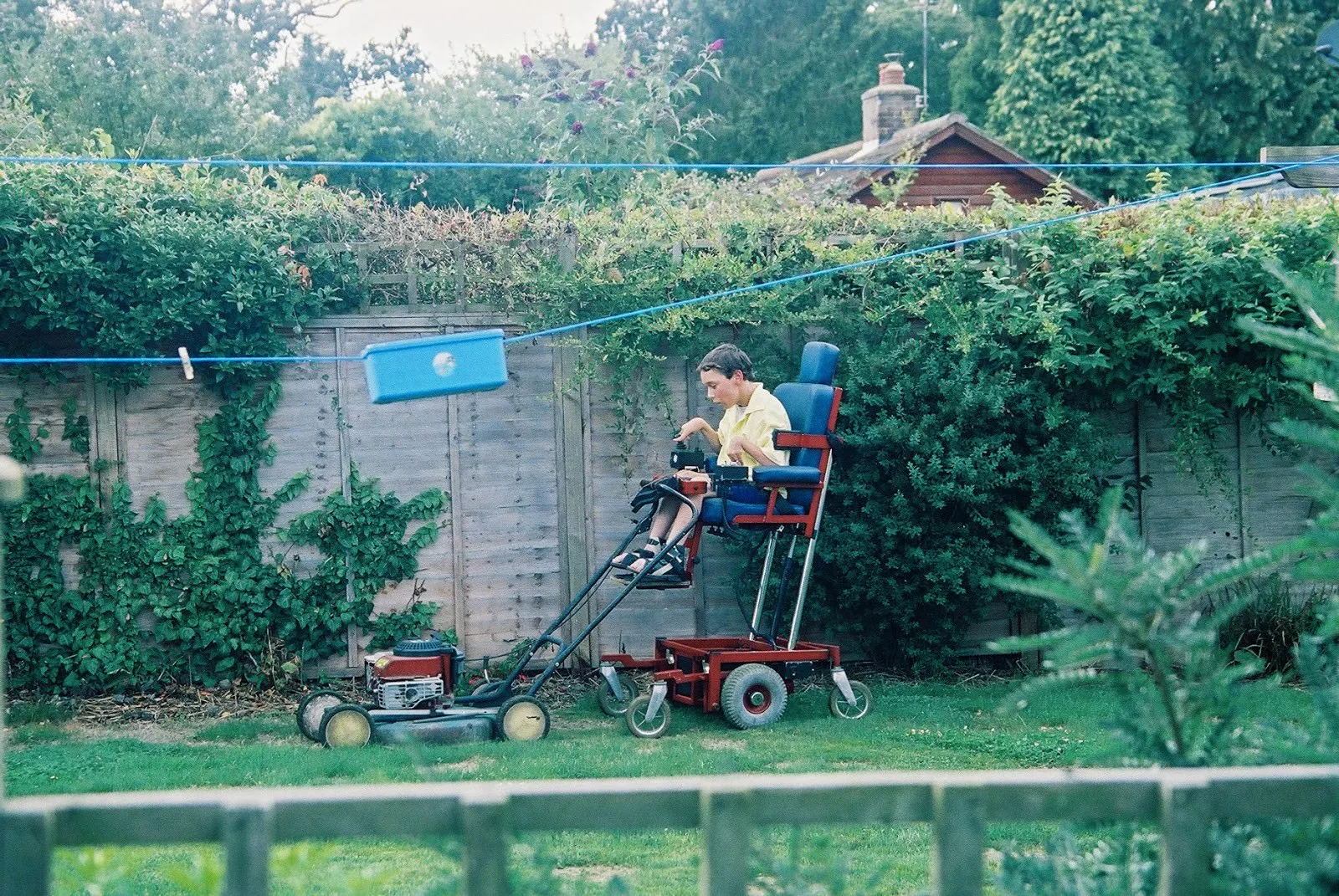 Jordan's brother Shane is using a lawn mower. It is attached to his motorised wheelchair that is raised quite high.