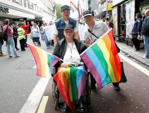 A group of people celebrating LGBTQIA+ Pride with rainbow flags.