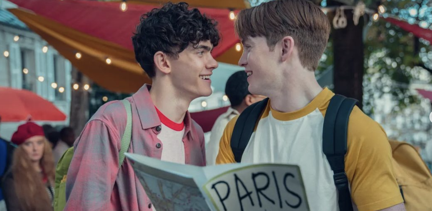 Two young men wearing backpacks smile at each other. One of them is holding a map with the title 'Paris'. 
