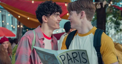 Two young men wearing backpacks smile at each other. One of them is holding a map with the title 'Paris'.