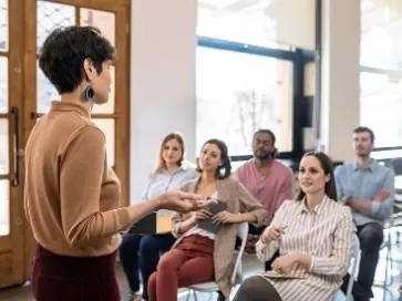 A woman at the front of a room, teaching a group of people.