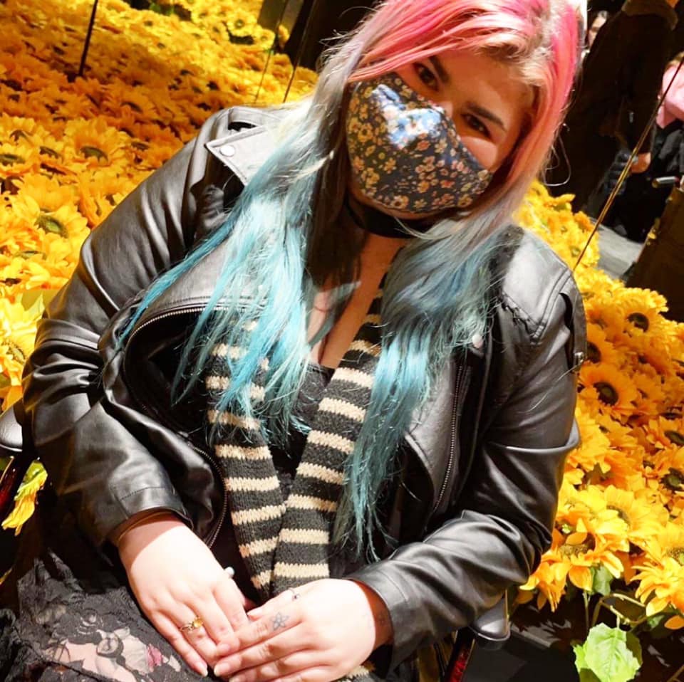 Zoe is wearing a mask and is seated with her hands cupping 