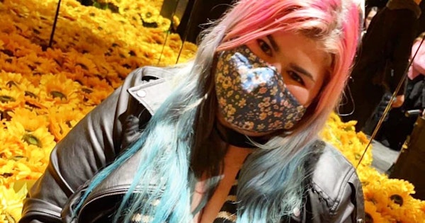 Zoe is wearing a mask and is seated with her hands cupping