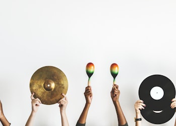 Five sets of hands holding up different instruments. Guitar, cymbal, maracas, vinyl records and drum sticks.