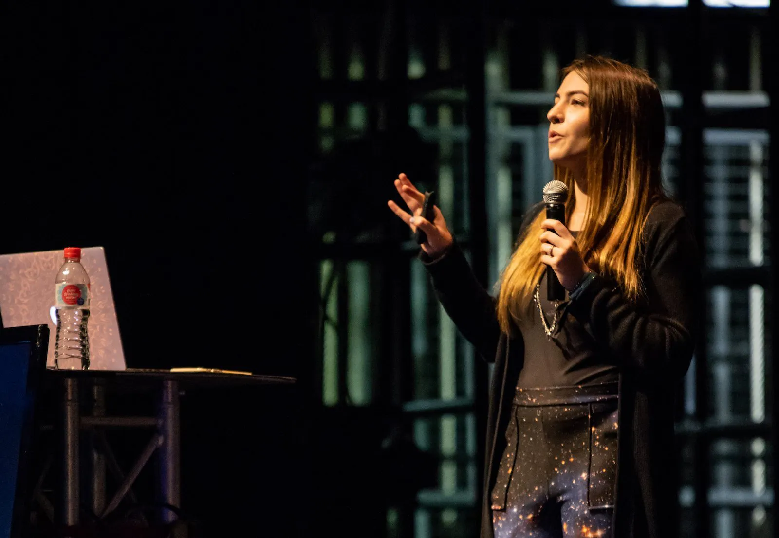 Mandy is presenting at a conference. She has a microphone in hand and is holding her right hand into the air.