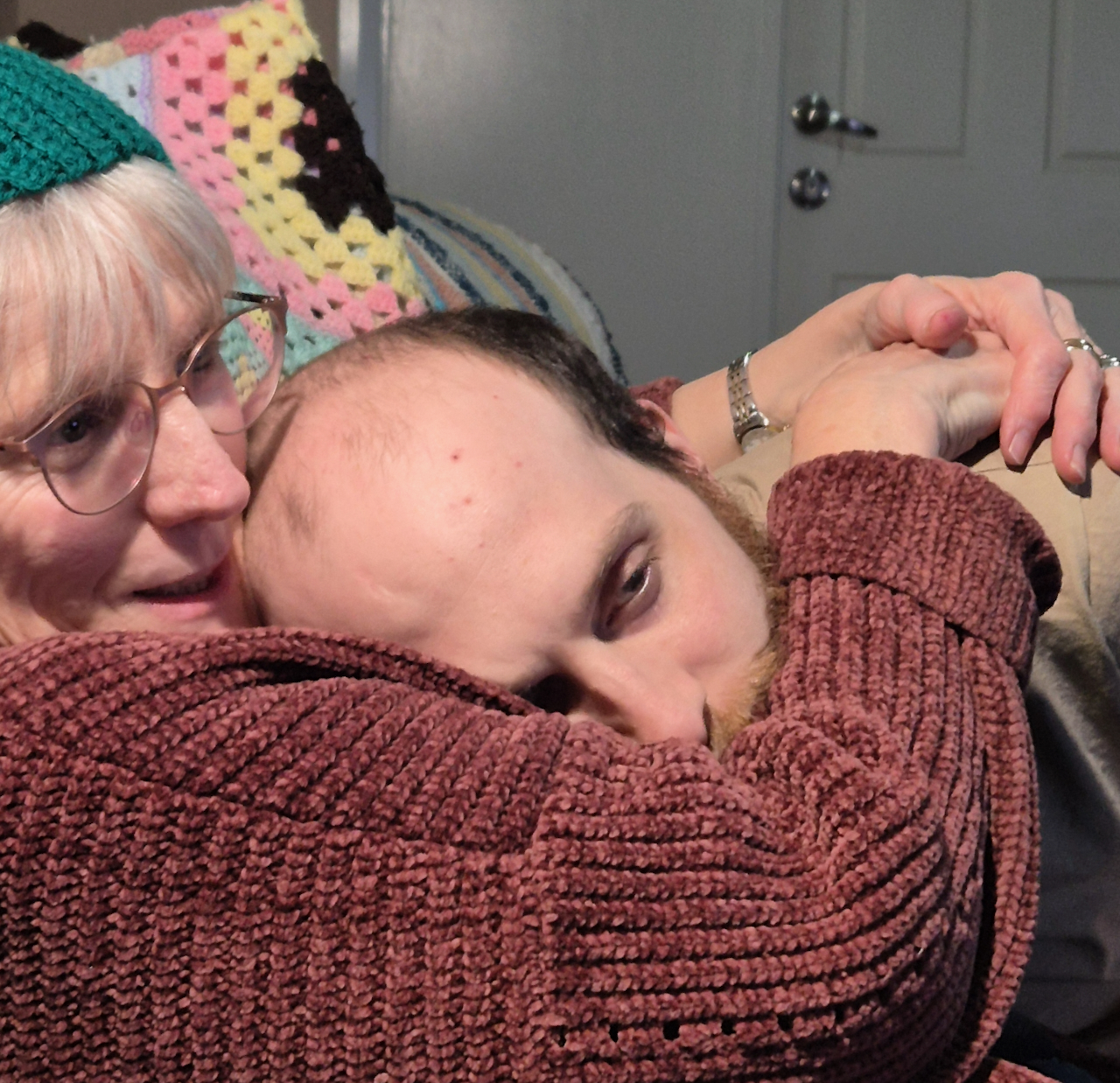 Dimity wears a red cardigan and hugs her son Stu, a Hireup client. 