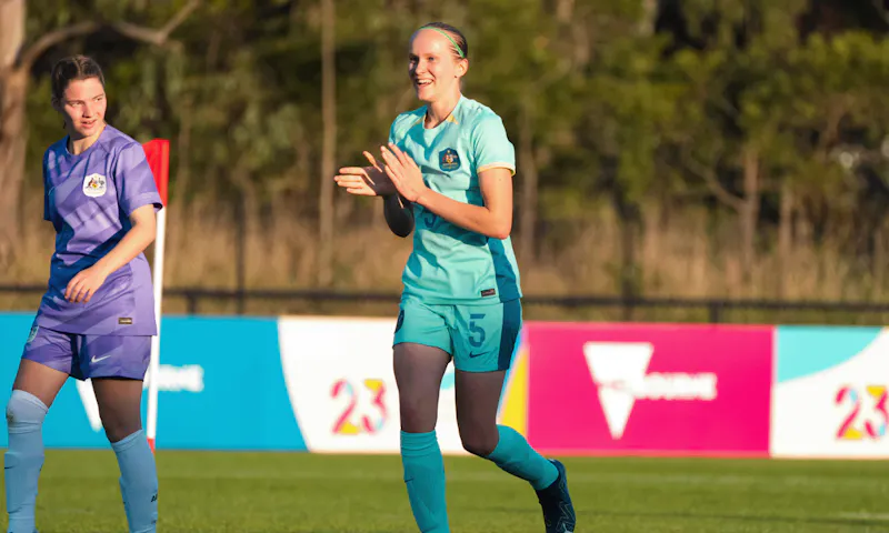 Athlete, Tamsin, is clapping in celebration on a soccer field. Tamsin wears her soccer uniform.