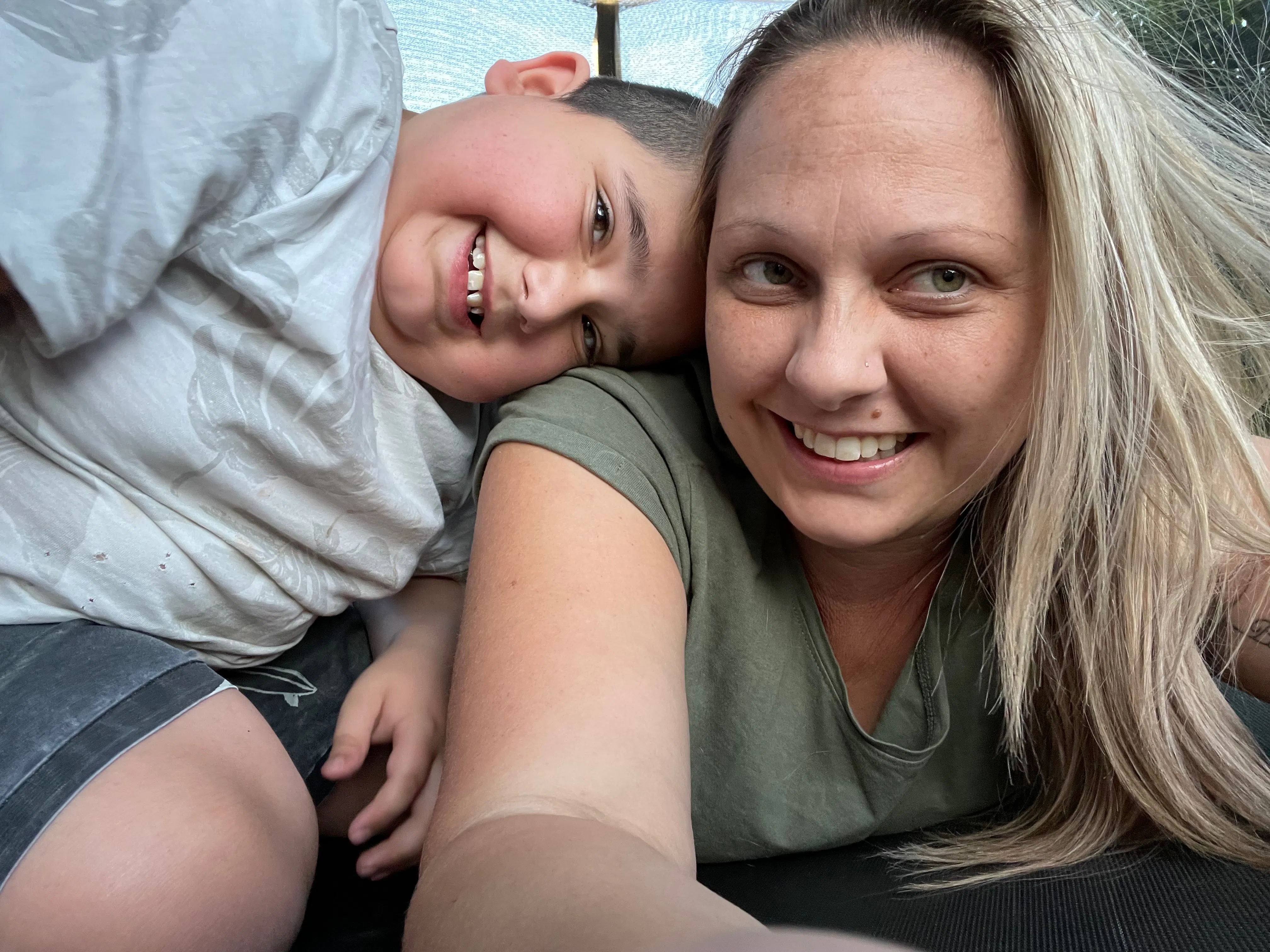 Amy is lying on a trampoline while her son, Luka, is resting his head on her shoulder. They're both smiling.