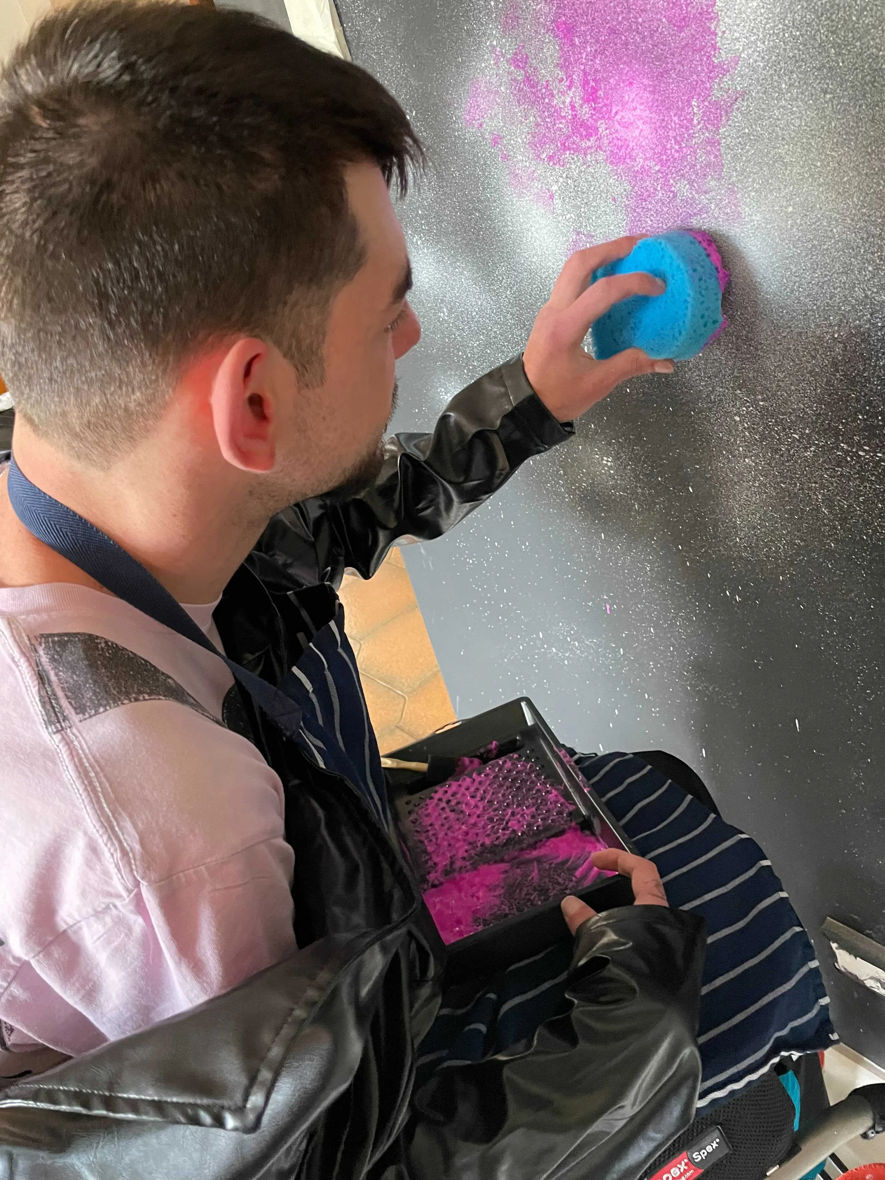 Andrew is applying the nebula to the mural with pink paint on a sponge.