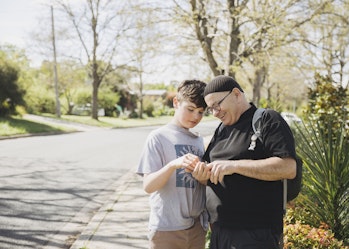Hireup client Zeph and his support worker Marcin are standing on a street pavement. Marcin is holding something in his hand, and both are smiling and inspecting it.